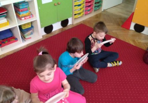 Dzieci siedzą na dywanie. Zlizują miód z papierowych talerzyków
